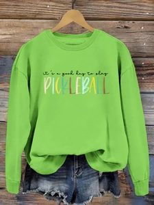 Detail of lime green sweatshirt with colorful pickleball slogan print on wooden hanger