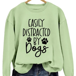 Mint green pullover sweatshirt featuring Easily Distracted by Dogs print on light wooden hanger