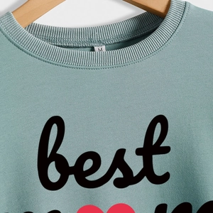 Sage green crewneck sweatshirt with Best Mom Ever embroidery and heart detail on wood hanger