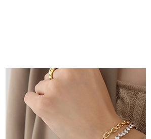 Gros plan de bracelets chaîne dorés et bracelet tennis en cristal avec bague dorée