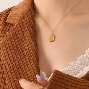 Goldene rechteckige Halskette mit Rosenrelief getragen von Model im Winteroutfit