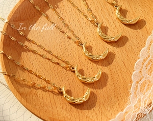 Macro shot of five gold hammered crescent moon pendants on sequin chains over wood