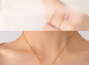 Détail d'un collier à billes dorées porté par un mannequin au style minimaliste moderne