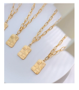 Détail du collier trombone doré avec pendentif rectangulaire au visage abstrait