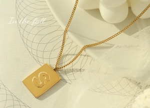 Close-up of gold-plated square pendant with embossed letter S on a thin curb chain