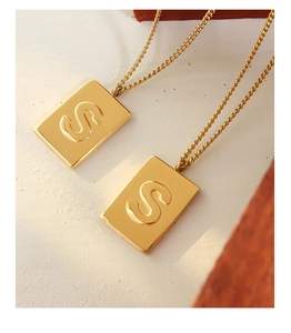 Macro detail of 18K gold plated square pendant necklace with engraved letter S on stone