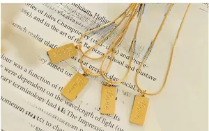 Detailed view of four gold Love rectangular pendants on snake chains over book pages