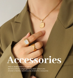 Détail du collier pendentif pissenlit vintage et bagues dorées sur blazer olive