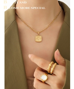 Détail du pendentif carré plaqué or 18K et des bagues sur un mannequin en blazer vert
