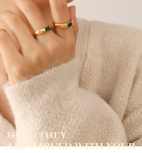 Detail of 18K gold plated rings with emerald green zircon on a beige knit sweater