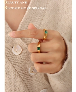 Detail of two 18K gold plated rings with emerald green zircon on a knit sweater