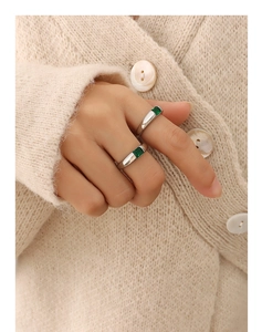 Detail of two silver titanium rings with emerald-cut green zircon on a knit cardigan background