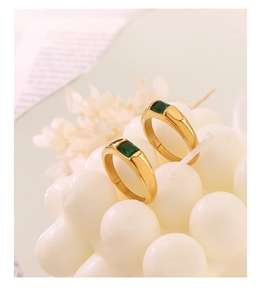 Close-up of two gold titanium rings with rectangular green zircon stones on white decor