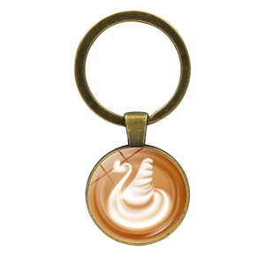 Bronze keychain featuring round glass pendant with swan latte art on white background