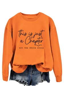 Close-up of printed quote on orange crewneck sweatshirt and denim shorts