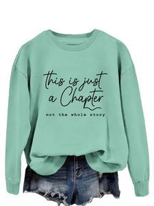 Detail of mint green sweatshirt featuring black printed slogan this is just a chapter