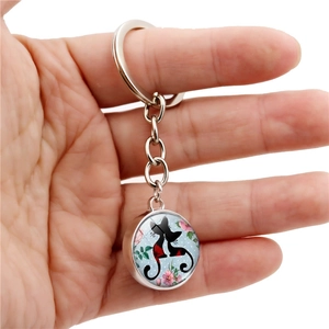 Silver metal keychain with round black cat glass pendant held by a hand over white background