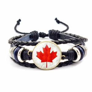 Detailed macro of a multilayer braided leather bracelet featuring a red maple leaf charm