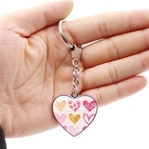 Romantic heart keychain with pink patterns and silver ring held against white background