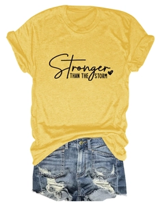 Detail view of yellow Stronger Than The Storm t-shirt paired with ripped denim shorts