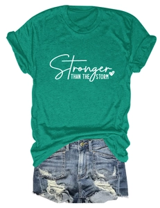 Flat lay of green t-shirt with Stronger Than The Storm text and ripped denim shorts