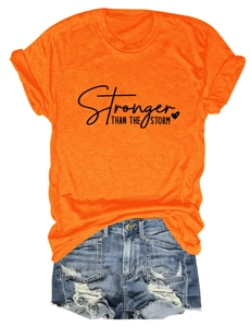 Flat lay of an orange cotton T-shirt with 'Stronger THAN THE STORM' text and ripped denim shorts