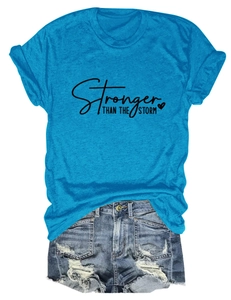 Flat lay of a blue T-shirt with 'Stronger Than The Storm' and distressed denim shorts