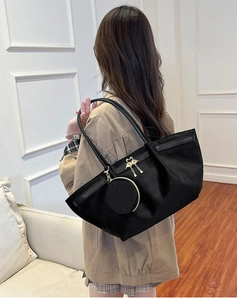 Detail of black tote bag with swan metal charm and small zipper pouch attachment