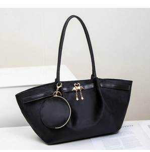 Detail of black suede tote bag featuring a gold swan charm and mini round purse attachment
