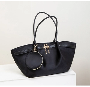 Detail of black suede tote bag with golden flamingo charm and round coin purse attachment