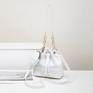 Sac seau blanc avec chaîne dorée et petit porte-monnaie rond assorti sur un socle minimaliste