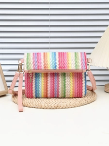 Close-up of colorful striped woven crossbody bag with pink leather strap on straw mat