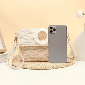 Woven straw crossbody bag with white daisy buckle and chain strap on decorative background