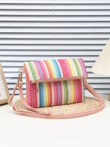 Detail of colorful woven envelope bag with pink adjustable strap on a rustic straw mat