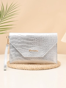 Detail of silver crocodile pattern clutch bag with gold logo on a beige background