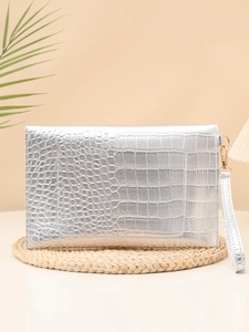 Detailed view of silver crocodile embossed leather clutch bag on a textured mat