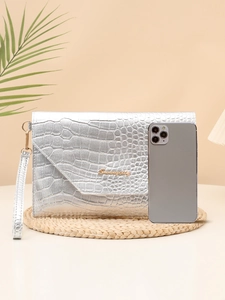 Silver crocodile texture clutch bag with golden logo shown next to a smartphone for size