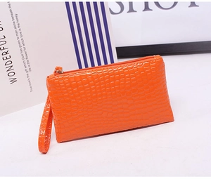 Detail view of a bright orange wristlet bag with crocodile pattern and zipper closure