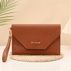 Brown envelope clutch bag with V-flap design and gold logo on a natural woven mat