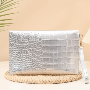 Silver crocodile texture clutch bag with wristlet strap on a rustic decorative mat