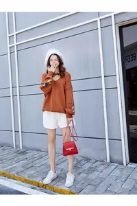 Close-up of bright orange-brown knit sweater featuring colorful floral embroidery on sleeves