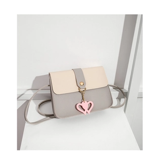 Detail of a minimalist two-tone crossbody bag with a pink double-heart charm accessory