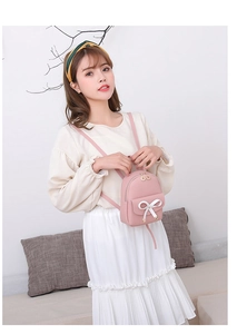 Mini pink PU backpack with white bow detail worn by woman in white pleated skirt