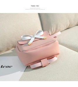 Pink PU leather mini backpack with a white bow detail and golden accents on a soft sofa