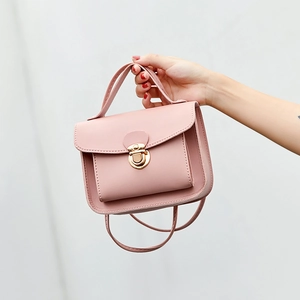 Pink faux leather crossbody bag with round gold lock and top handle held by hand
