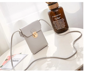 Détail d'une pochette téléphone en cuir PU gris avec fermoir doré sur une table blanche