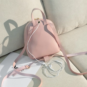 Pink leather mini backpack with bow detail and headphone jack on beige fabric sofa