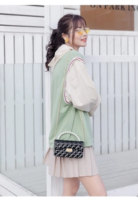 Detail shot of black quilted bag with pearl handle and golden chain on a green outfit