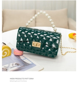 Detail of dark green quilted jelly bag with pearl handle and golden chain on table