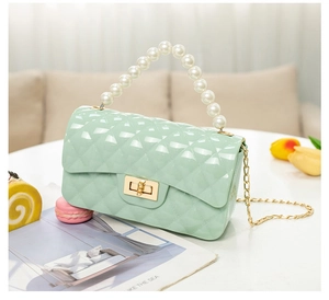 Detail of mint green jelly bag with quilted texture, pearl handle, and gold chain strap